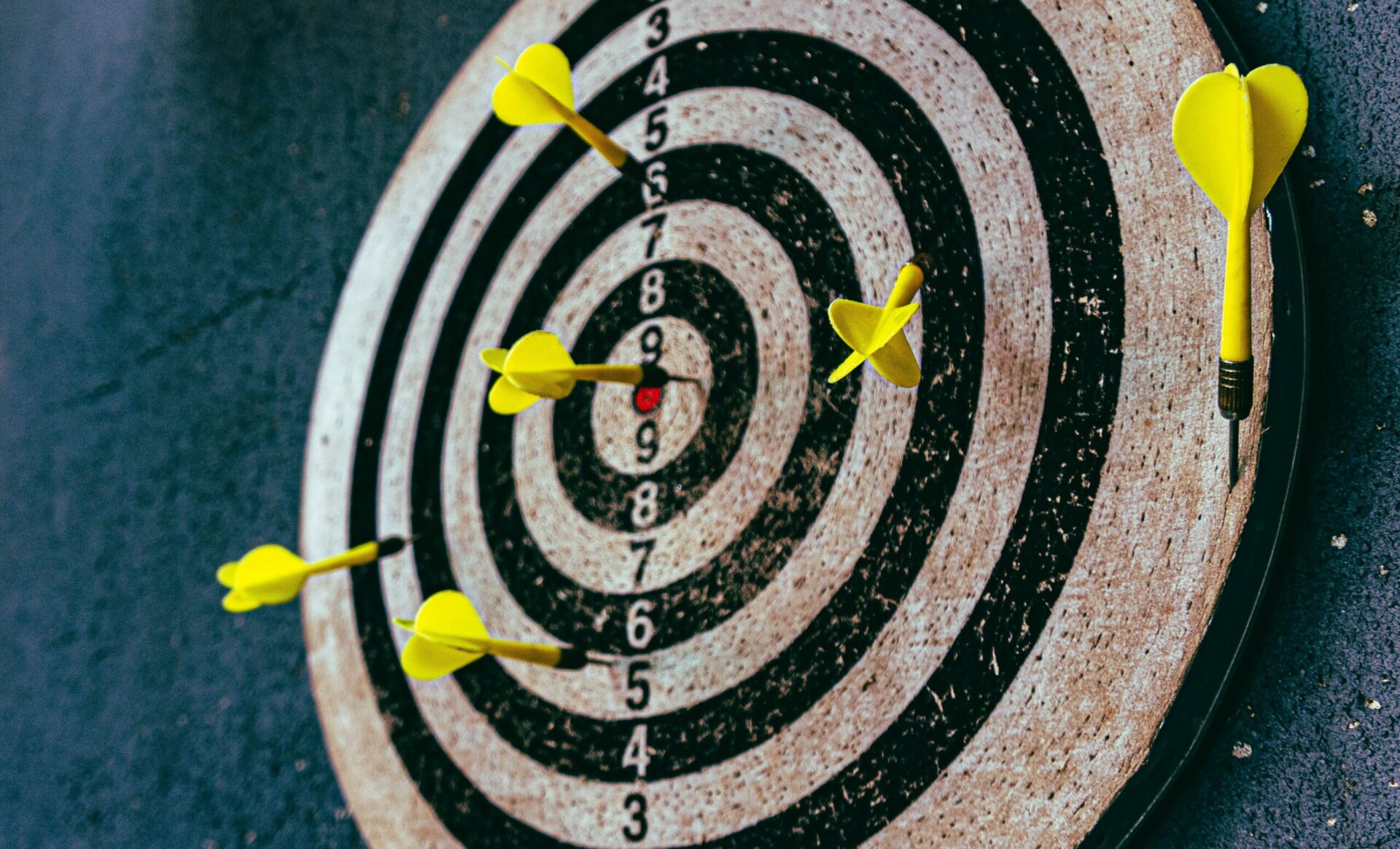 Photo of a black and white dart-board with yellow darts to depict the achievement of target goals