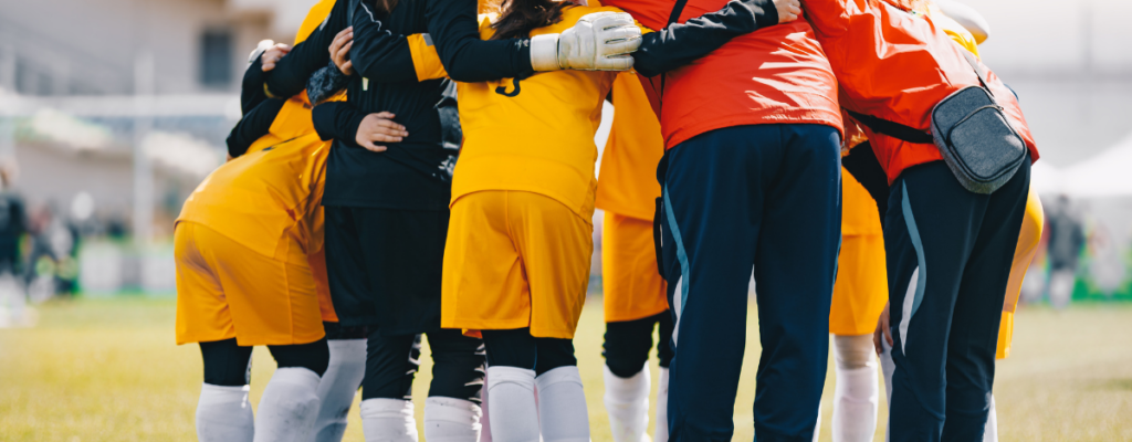 Coaches and youth team members in a huddle in an outdoor stadium.