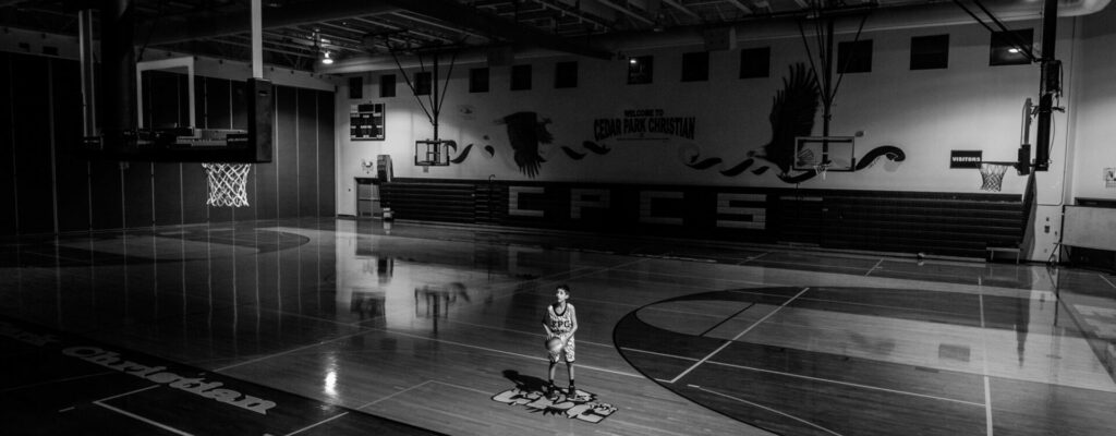 boy playing basketball in empty gym