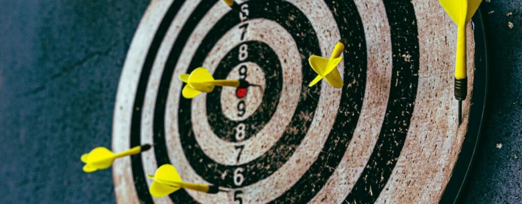 Photo of a black and white dart-board with yellow darts to depict the achievement of target goals